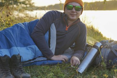 Genç turist doğada uyku tulumunda dinleniyor. Uyku tulumu çimenlerin üzerinde yatıyor.