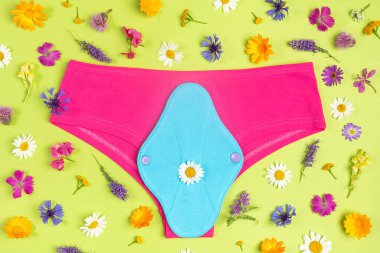 Yeniden kullanılabilir mavi regl yastığı ve yeşil arka planda doğal çiçekli pembe iç çamaşırı. Sağlık ve sıfır atık, plastik yok, çevre dostu konsept. Üst Görünüm Düz
