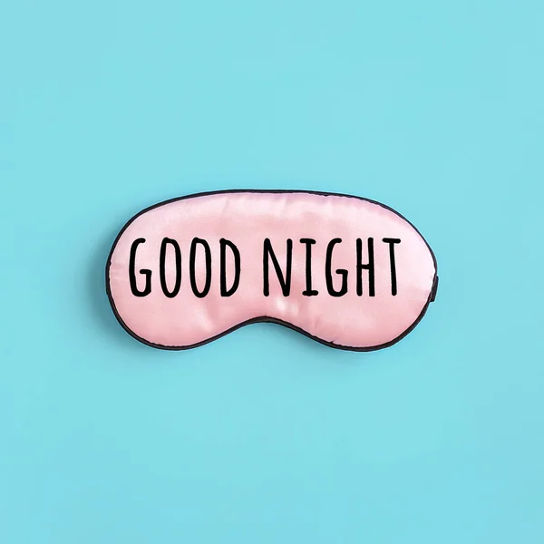 青い背景に目のためのピンクの絹の睡眠マスクの良い夜のテキスト トップビューフラットレイ 良い睡眠とメラトニン産生のための光からの概念的な目の保護 — ストック写真