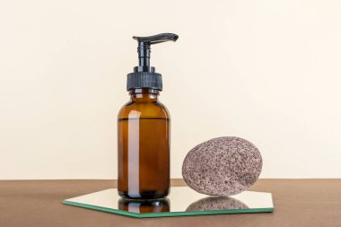 Brown glass bottle with pump of cosmetic products and stone on mirror, beige and brown background. Natural Organic Spa Beauty Cosmetic concept Mockup.