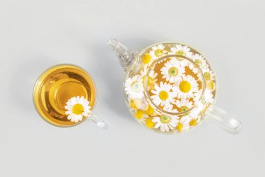 Bir fincan çay ve sarı arka planda papatya çiçekli şeffaf çaydanlık. Papatya çayı sağlığınıza iyi gelir. Üst Manzara. Moda Renkleri 2021.