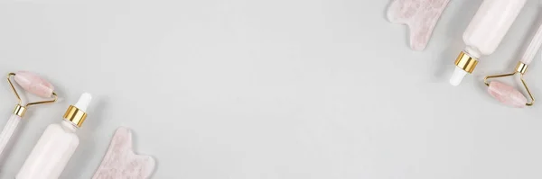 クリスタルローズクォーツ顔ローラー マッサージツールGuaの社とアンチエイジングコラーゲン 灰色の背景にガラス瓶の血清 自然なリフティングのためのフェイシャルマッサージ 美容コンセプトコピースペース バナー — ストック写真