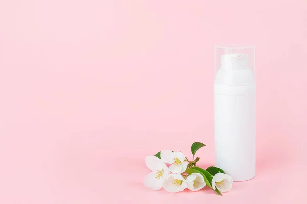 One white blank cosmetic tube bottle and flower, blooming branch on pink background. Natural Organic Spa Cosmetic Beauty Concept. Mockup Front view Copy space.