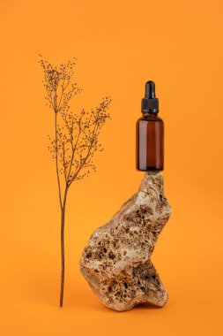 Kahverengi cam şişede taş üzerinde pipet ve turuncu arka planda kurutulmuş çiçekler bulunan serum ya da temel yağ. Doğal Organik Spa Kozmetik Konsepti.
