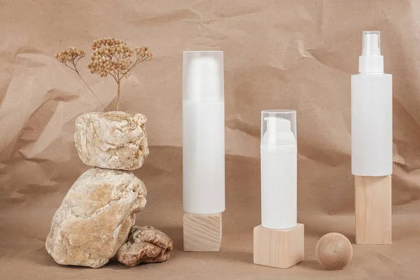 Three white blank cosmetic tube with cream, lotion or shampoo, stones, geometric shape, dried plant flowers on beige craft paper background. Natural Organic Spa Cosmetic.