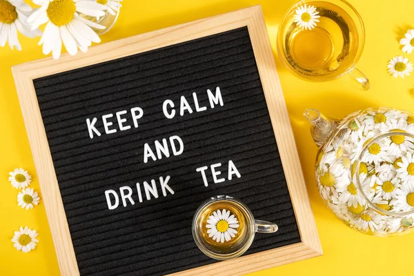 Keep calm and drink tea. Motivational quote on black letter board and herbal chamomile tea on yellow background. Concept inspirational quote of the day. Flat lay Top view.