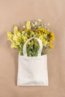 Bej arka planda kumaş eko torba içinde bir buket tarla çiçeği. Plastik ve sıfır atık kavramı. Üst Görünüm Modifiye.