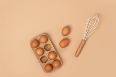Tahta yumurta kutusunda yumurtalar ve bej arka planda çırpma. Düz konum Üst Görünüm Kopyalama alanı.