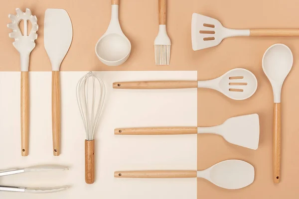 Pattern made from cooking utensil set. Silicone kitchen tools with wooden handle on beige background. Top view Flat lay.