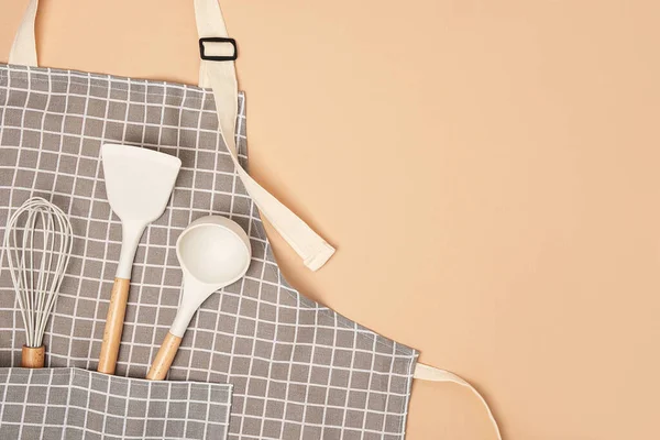 Cooking background. Flat kitchen accessories. Apron and silicone cooking utensil with wooden handle on beige background with copy space. Top view Flat lay.