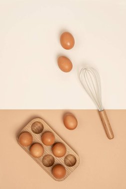 Tahta yumurta kutusunda yumurtalar ve bej arka planda çırpma. Düz konum Üst Görünüm Kopyalama alanı.
