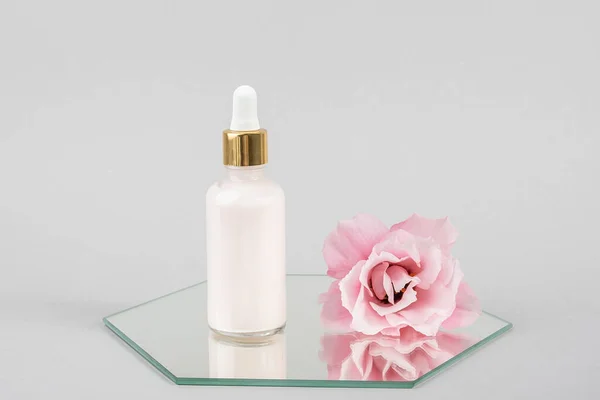 Una bottiglia di vetro contagocce e rosa bel fiore su specchio, sfondo grigio. Natural Organic Spa Cosmetic concept. Vista frontale — Foto Stock