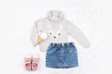 Beyaz arka planda günlük çocuk kıyafetleri, ayakkabıları ve aksesuarları. Moda kızı izci kitabı kutsaması. Örgü süveter, kot etek, spor ayakkabı, dondurma külahı. Üst manzara, düz uzanma.