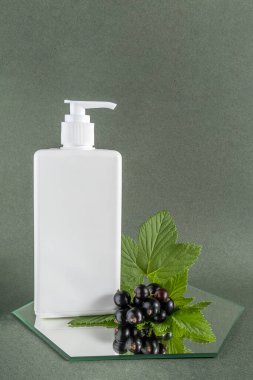 Aynada beyaz kozmetik boş şişe ve siyah frenk üzümü filizi, yeşil arka plan. Doğal organik güzellik kozmetik konsepti. Ön görünüm.