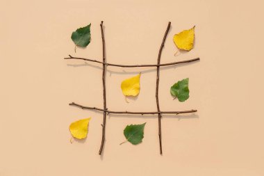 Yaratıcı sonbahar konsepti. Tic-tac-toe, yaz ve sonbahar arasında isim ve haçlar. Şebeke içinde dallardan yapılmış yeşil ve sarı yapraklar. Sonbahar kazandı. Üst Görünüm Düz.