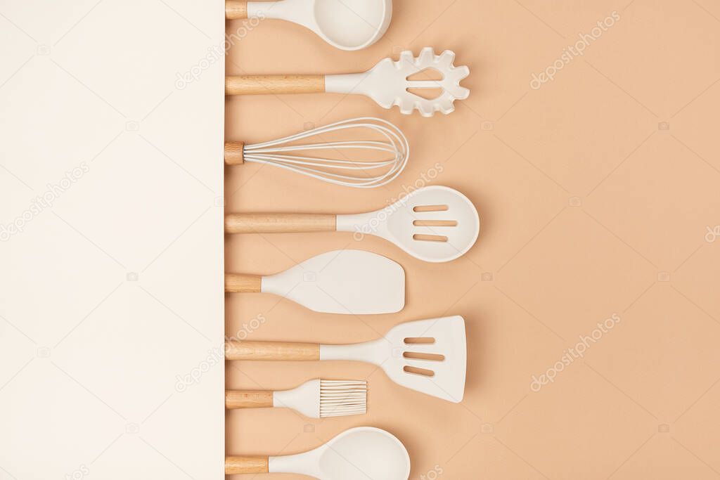 Cooking utensil set. Silicone kitchen tools with wooden handle on beige background with copy space. Top view Flat lay.