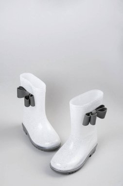 Gri arka planda fiyonklu beyaz parlak lastik yağmur botları ve kopya alanı.
