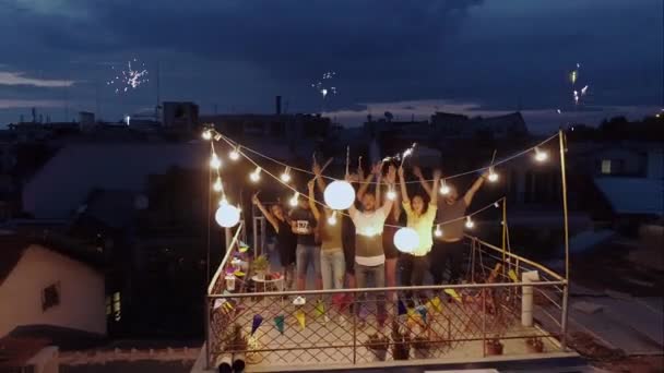 Silvesterfeuerwerk während der Mitternachtsparty der multi-ethnischen Gruppe junger Leute, die auf dem Dach feiern, Winken an der Drohne Halten Wunderkerze Feuer Festliche Zeit Happy Event Schöne Lichter Urbane Nacht — Stockvideo