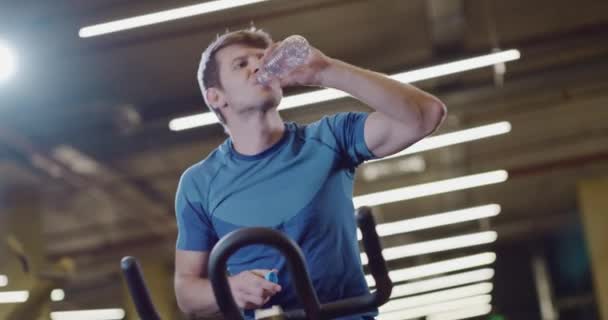 Jóképű Fitness Man Closeup Helyhez kötött kerékpár Gyakorlat Ivóvíz Sport Központ Funkcionális képzés Kitartás Egészség Fókuszált Fitness Concept 4k — Stock videók
