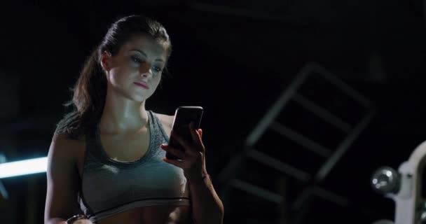 Красива атлетична жінка робить перерву після тренування використовуючи телефон в спортзалі Здоровий спосіб життя Відпочинок Фітнес-технологія концепція 4k — стокове відео