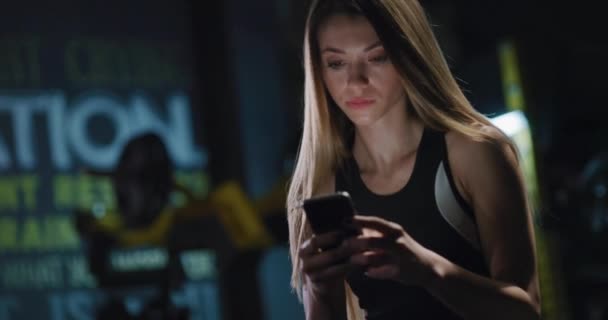 Молода жінка в спортивному одязі робить перерву після тренування використовуючи телефон крупним планом фітнес центр здоровий спосіб життя фітнес концепція 4k — стокове відео
