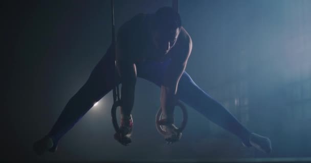 Knappe gespierde atletische man in de gymnastiek Uniform doet een split in intensieve training op gymnastische ringen close-up in de sportschool fysieke kracht inspanning gymnastiek concurrerende mentaliteit concept 4k — Stockvideo