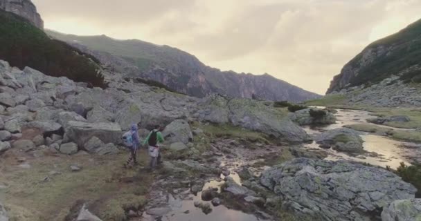 マウンテンバレーの美しいアルパインストリーム追跡と観光を通してカップルハイキングを通してフライト｜Epic Mountain Vacation Concept — ストック動画