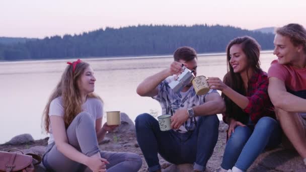 Aantrekkelijke multiraciale groep jonge vrienden zitten op het strand bij het meer 's morgens vroeg wakker worden en drinken koffie vakantie in de natuur recreatie concept slow motion schot op rode epische w 8k. — Stockvideo