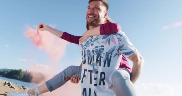 Glückliches Paar Mann tragen Frau auf dem Rücken am Strand Seeufer vorbei durch Rauchwolken romantisches Wochenende junge Liebe Konzept Zeitlupe Schuss auf roten epischen w 8k. — Stockvideo