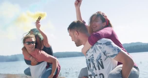 Jovens amigos homens e mulheres giram e riem no piggyback na costa do lago se divertir com o foguete de fumaça alcançar a felicidade conceito de família feliz câmera lenta tiro no épico vermelho w 8k. — Vídeo de Stock