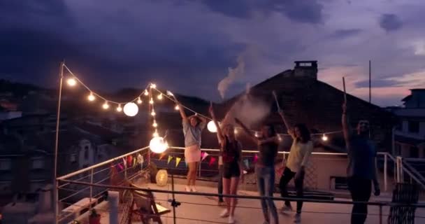 Vol de drone au-dessus du toit Divers jeunes gens de partie saluant au drone tenant le feu scintillant Fête de la Saint-Sylvestre Festive Time Happy Event Concept pendant la belle nuit urbaine — Video