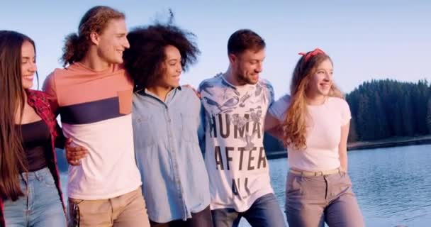 Szczęśliwa młoda grupa przyjaciół chodzić i śmiać się na brzegu jeziora wav ręce przygoda w lesie nastolatek życie przygoda koncepcja slow motion shot on red epic w 8k. — Wideo stockowe