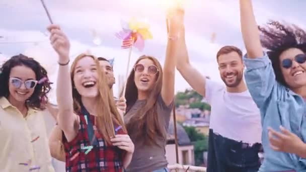 Divers groupes de jeunes hipsters amis sur le toit soulevant le feu scintillant dans les airs dans la fumée colorée riant et dansant dans les confettis belle jeunesse temps festif heureux concept d'événement au crépuscule — Video