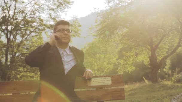 Boldog üzletember beszélő telefon Park pad természet nap háttér — Stock videók