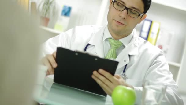 Młody lekarz oferuje owoce zielone jabłko pacjentki — Wideo stockowe