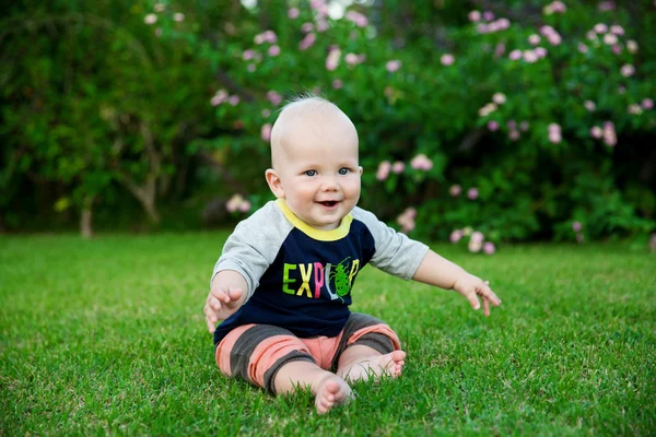 Feliz menino adorável sentado na grama — Fotografia de Stock