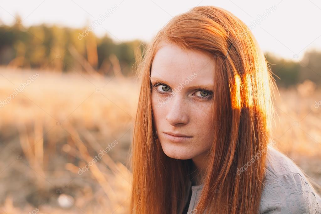 Beauty Young Woman with Red Hair in Golden Field at Sunset.