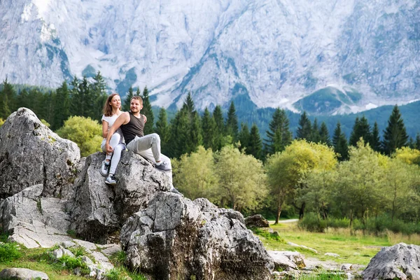 Couple of travelers on the Lago di Fusine lake with Mangart mountains in the background. — Stock Photo, Image