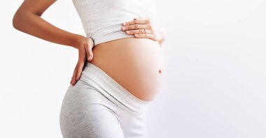 Hamile kadın, beyaz arka planda göbeğinin üstünde el ele tutuşuyor. Hamileliğin güzel fotoğrafı. Anne bebeği bekliyor. Kadınlar hamileliğe hazırlanır. Doğum öncesi dönem kavramı, annelik sağlığı.