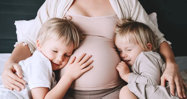 怀孕妇女和她的孩子在床上休息 可爱的母亲和幼儿一起呆在家里 小孩子们牵着妈妈怀孕的肚子 第三次怀孕母亲 养育子女的概念 — 图库照片