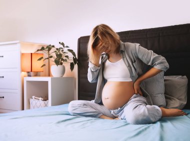 Hamile kadın sırt ağrısı ya da baş ağrısı çekiyor. Kadının evinde kasılma ve sırt ağrısı var. Hamilelik kavramı, jinekoloji.