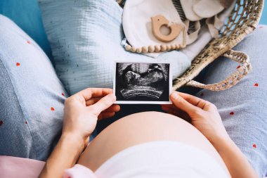 Hamile kadın ultrason görüntülerine bakıyor. Müstakbel anne hamilelik sırasında bebek doğumu için bekliyor ve hazırlanıyor. Yeni doğan çocuk için hasır sepetli bir anne..