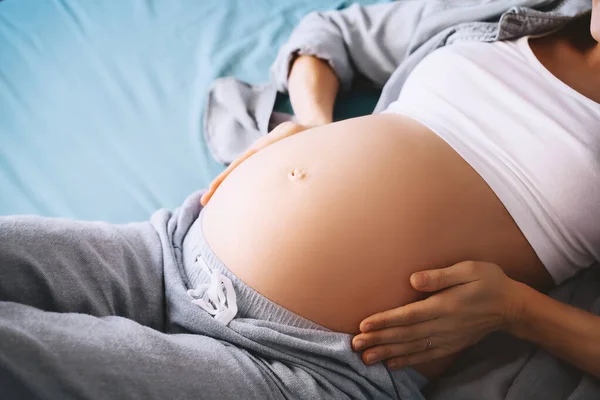 对躺在床上的漂亮孕妇的小腹进行特写 准妈妈抱着肚子休息 可爱的母亲在等着孩子怀孕 妇科概念 — 图库照片