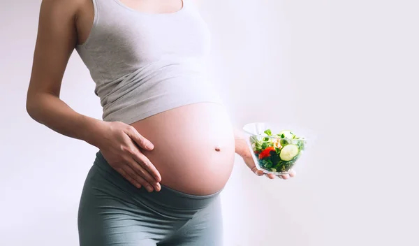 妊娠中の女性は葉酸を含む健康食品を食べる B9ビタミン クローズアップ妊娠中の女性の腹と野菜サラダ 妊娠中の出生前栄養 健康的なライフスタイルと食事の概念 — ストック写真