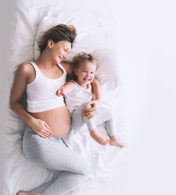 Hamile anne ve kızı evde dinleniyor. İkinci hamileliği sırasında ilk çocuğu olan genç bir kadın. Annelik ve ebeveynlik kavramı. Küçük kız ve anne. Mutlu aile bebek bekliyor..