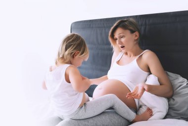 Hamile anne ve kızı evde dinleniyor. İkinci hamileliği sırasında ilk çocuğu olan genç bir kadın. Annelik ve ebeveynlik kavramı. Küçük kız ve anne. Mutlu aile bebek bekliyor..