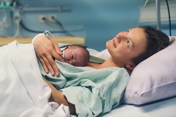 Anne ve yeni doğan. Doğum hastanesinde doğum. Genç anne doğumdan sonra bebeğine sarılıyor. Doğum yapan kadın. Doğumdan sonra bebek hayatının ilk anları.