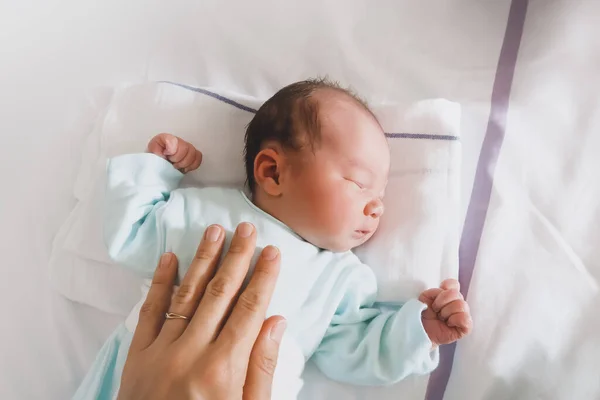 Mother and newborn resting after childbirth in maternity hospital room. Mother hugging her sleeping newborn baby.