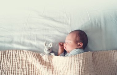 Yeni doğmuş bebek hayatının ilk günlerinde uyur. Yeni doğmuş bir çocuğun portresi. Bir haftalık. Bez arka planda beşikte şirin yumuşak bir oyuncak ile huzur içinde uyuyor..