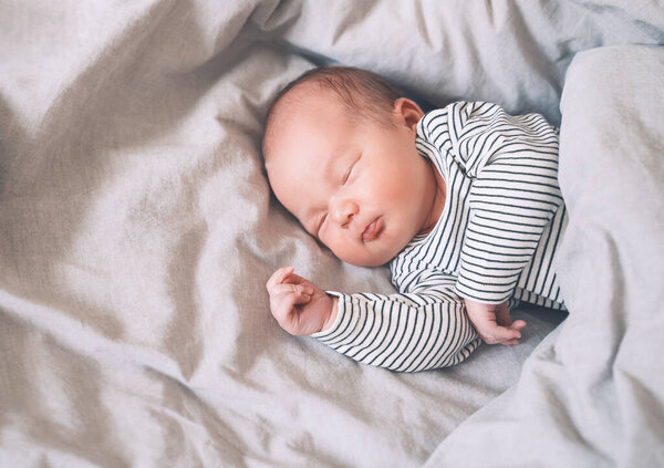 Сон новорожденного ребенка в первые дни жизни. Портрет новорожденного мальчика недельной давности, мирно спящего в кроватке на фоне ткани.